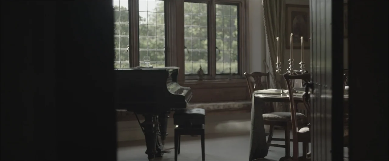 Behind the Line: Escape to Dunkirk (2020) movie still: medium — A traditional room features a black grand piano beside a large leaded window. An…