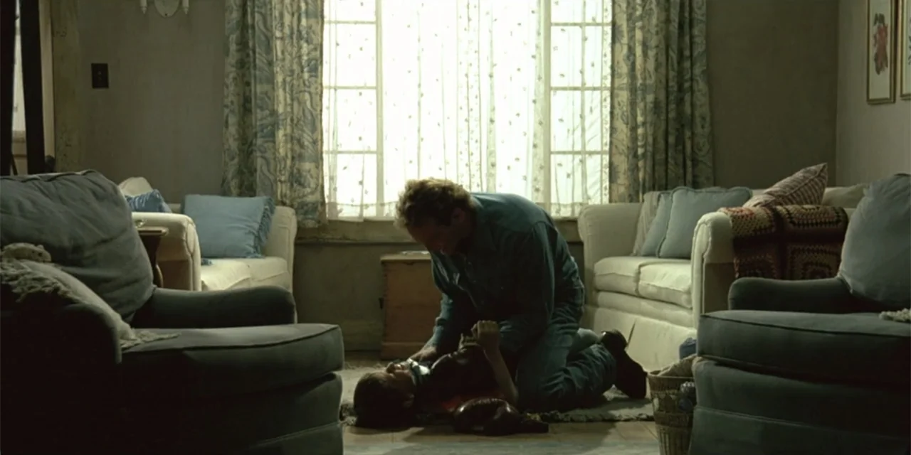 El sótano (2024) movie still: wide — A traditional residential living room contains two upholstered armchairs and a matching sofa set. A man kneels…