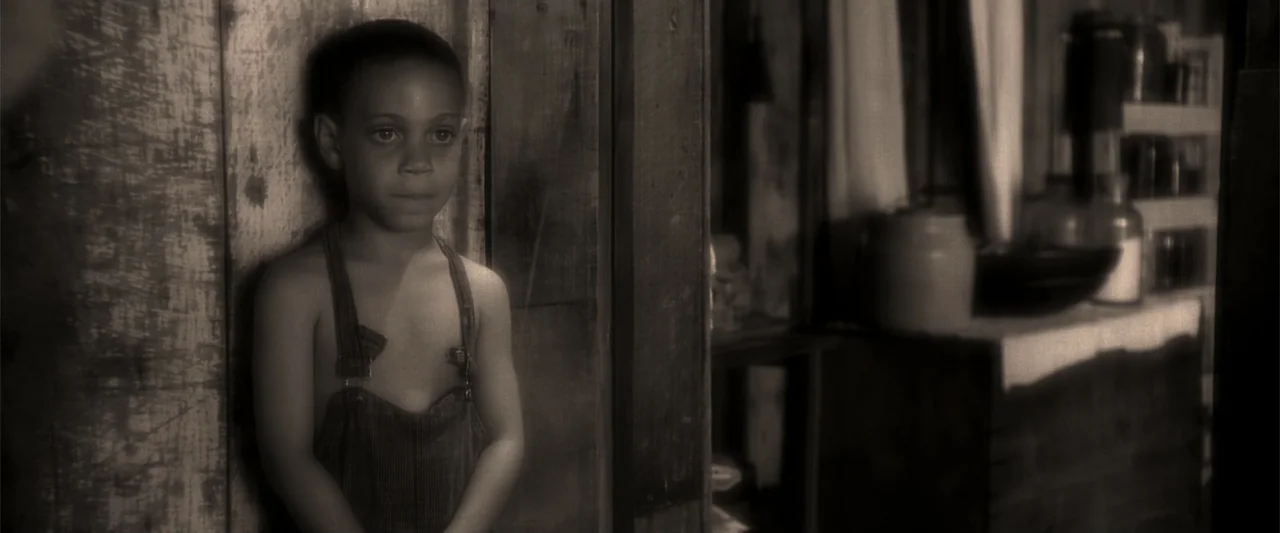 A Family Thing (1996) movie still: medium — A rustic shack interior features worn wooden walls and a blurred shelf with jars. A young boy stands…