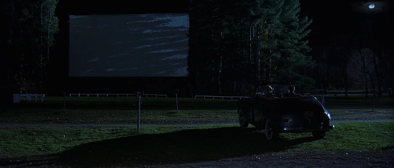The Cider House Rules movie still: wide — A drive-in theater at night features a large blank white projection screen. A vintage convertible is…