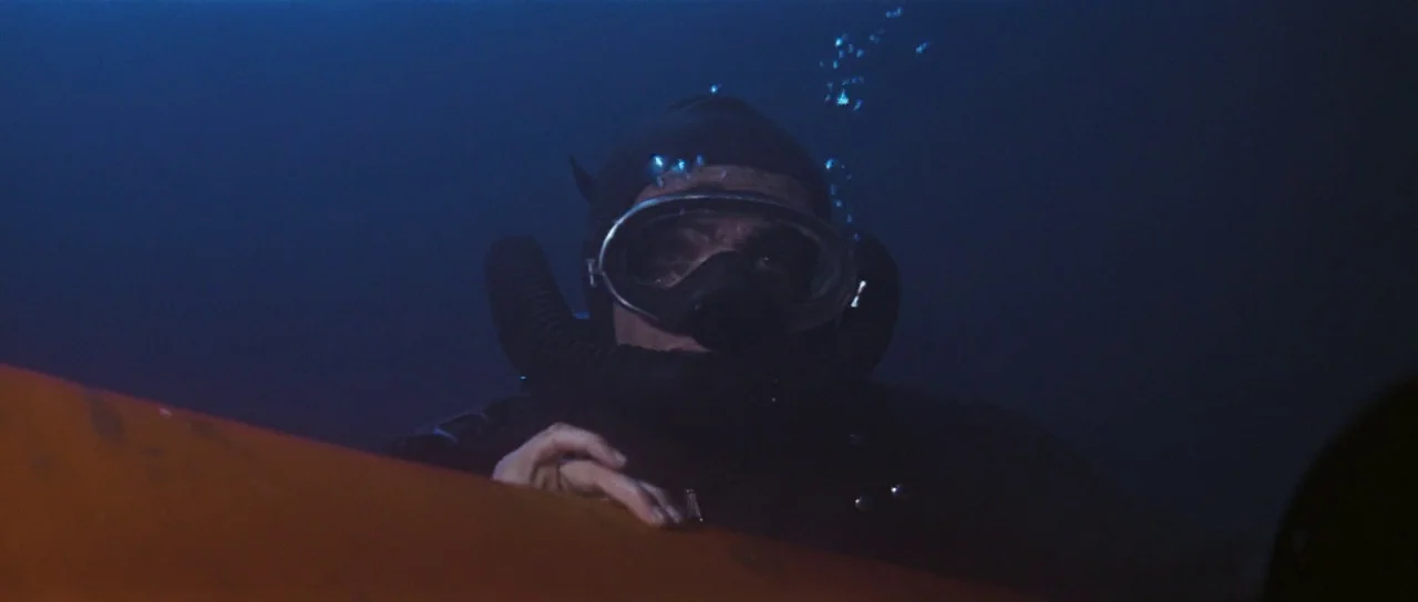 Thunderball (1965) movie still: closeup — A person in a black wetsuit surfaces in dark, cold water at night. The diver holds onto a bright orange…