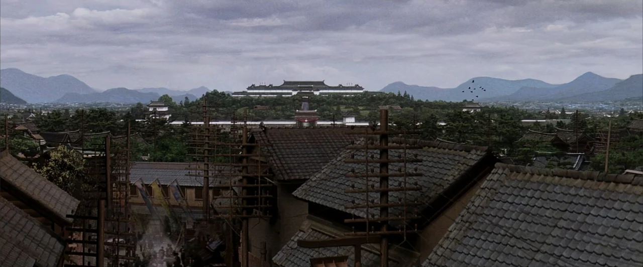The Last Samurai (2003) movie still: establishing — A Japanese town with traditional tiled roofs sits nestled below a distant hilltop palace. Clouds…