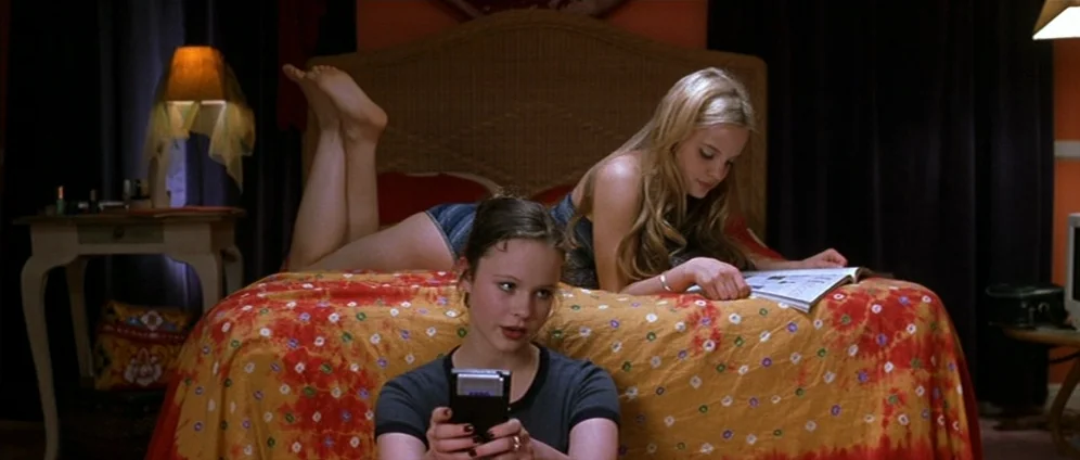 American Beauty (1999) movie still: medium — A dimly lit room with an orange patterned bedspread and dark curtains. Two teenagers occupy the space…