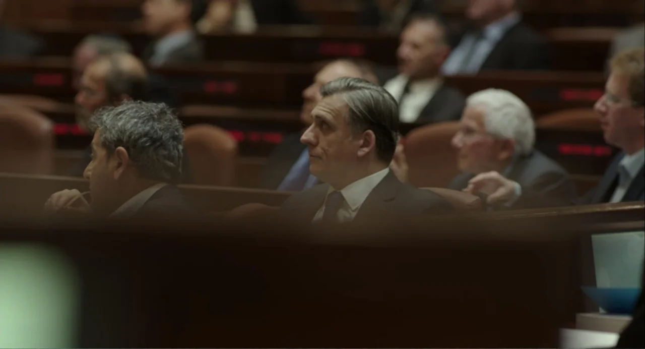 Norman: The Moderate Rise and Tragic Fall of a New York Fixer (2016) movie still: medium — A crowded legislative or corporate hall with tiered…