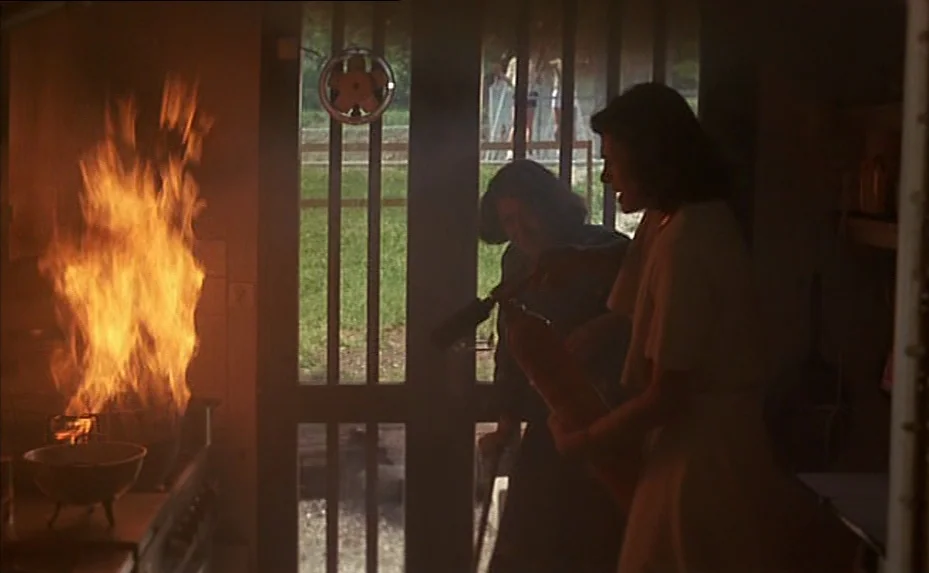 The Woman Next Door (1981) movie still: medium — A dark, shadowed room features a bright fire burning in a stove on the left. Two women in the room…
