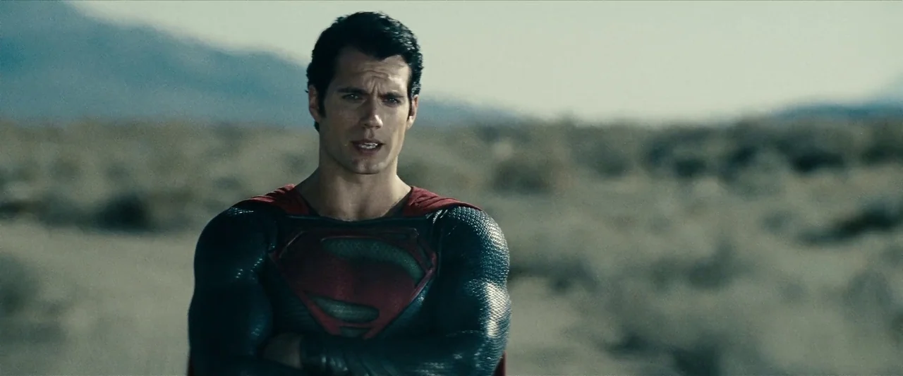 Man Of Steel (2013) movie still: medium — A vast, arid desert landscape stretches out behind a man in a superhero costume. The man stands with arms…