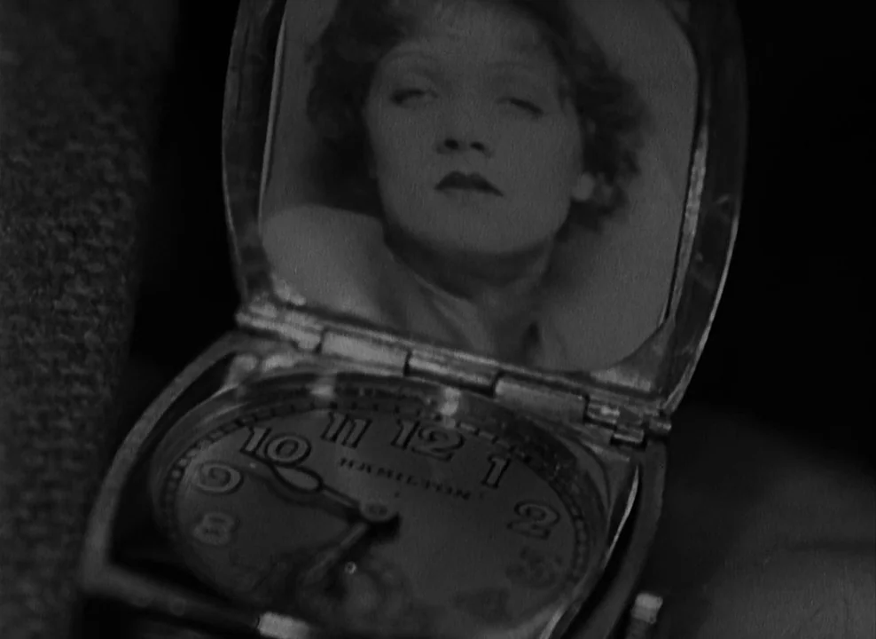 Shanghai Express (1932) movie still: closeup — A vintage pocket watch with a Hamilton watch face is held open. A small portrait of a woman is fixed…
