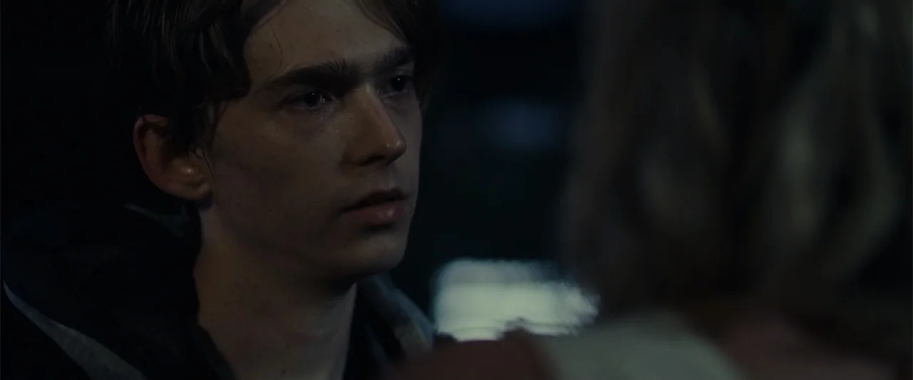 Chemical Hearts (2020) movie still: closeup — A dimly lit environment with shadows obscuring most architectural details. A young man listens to…