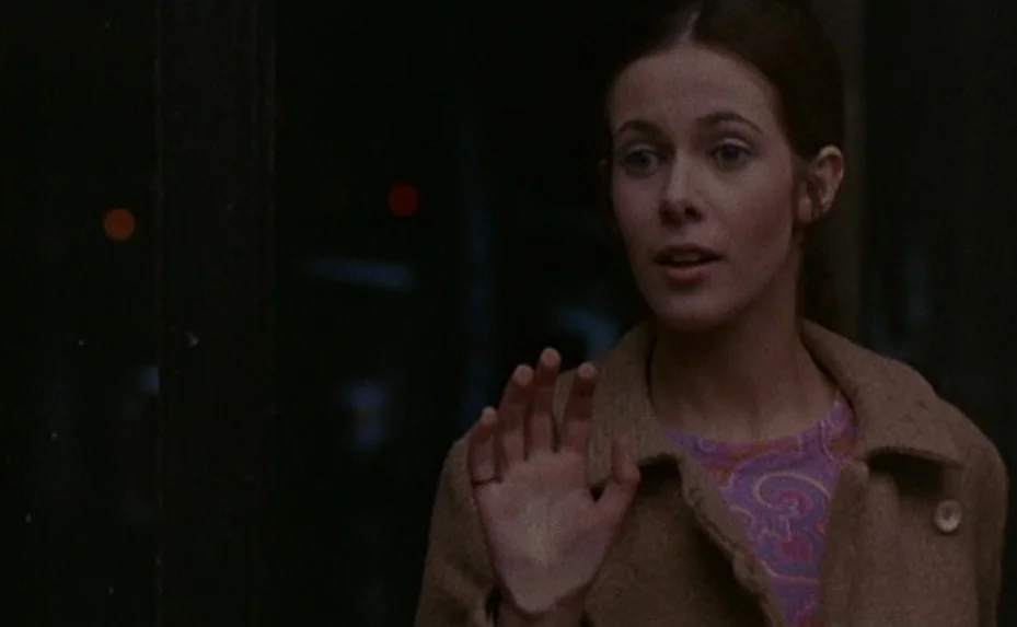 Love on the Run (1979) movie still: medium — A woman stands behind a large dark glass surface looking into the night. She rests her hand against the…