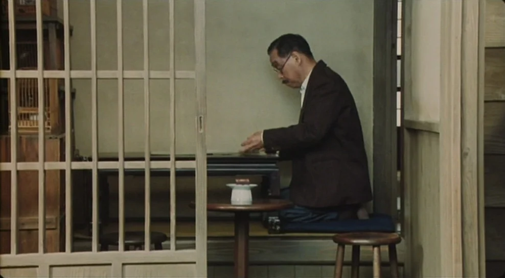 Madadayo (1993) movie still: medium — A traditional Japanese room features sliding lattice wooden doors and tatami flooring. An older man kneels on…