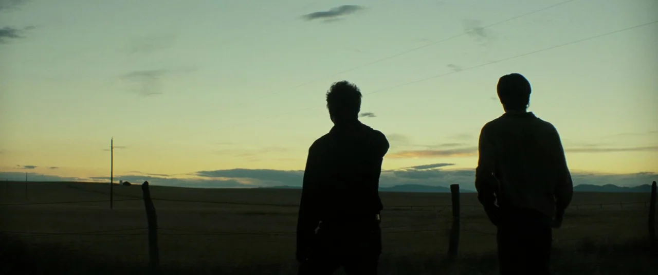 Hell or High Water (2016) movie still: wide — A desolate rural landscape at twilight features dry grass and thin barbed wire fences. Two men stand…