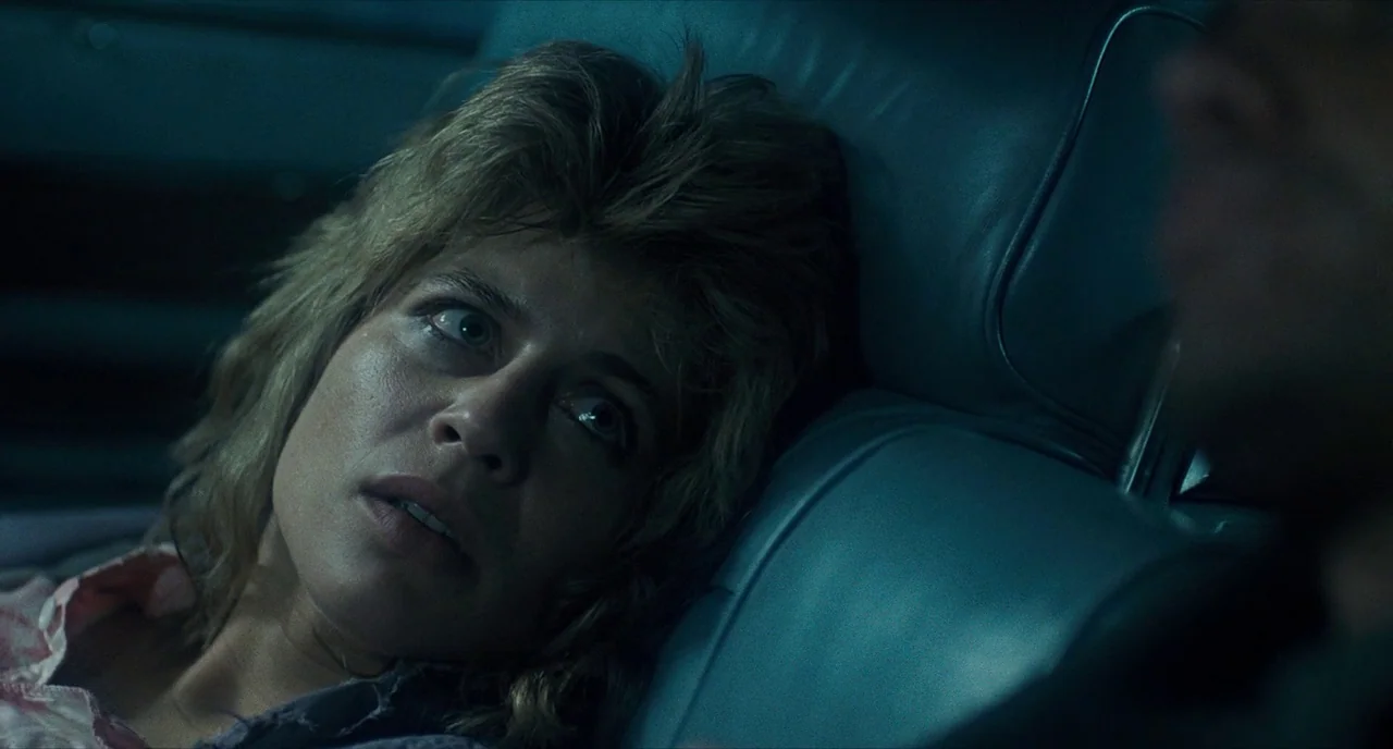 The Terminator (1984) movie still: closeup — The interior of a car at night is lit by ambient blue light. A woman rests her head on the seat cushion…