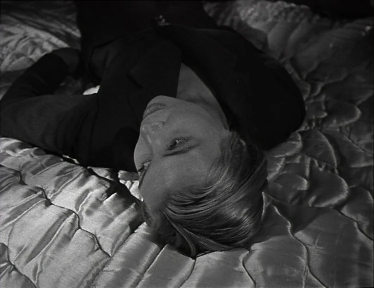 La Pointe Courte (1955) movie still: closeup — A person lies on a quilted, satiny fabric surface that fills the frame. The subject is positioned on…