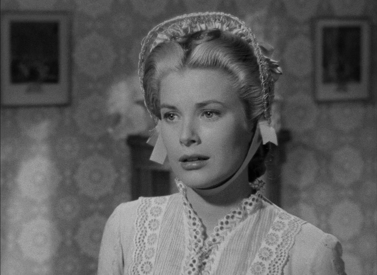 High Noon (1952) movie still: closeup — A domestic space features patterned wallpaper and framed pictures in the background. A woman in a lacy…