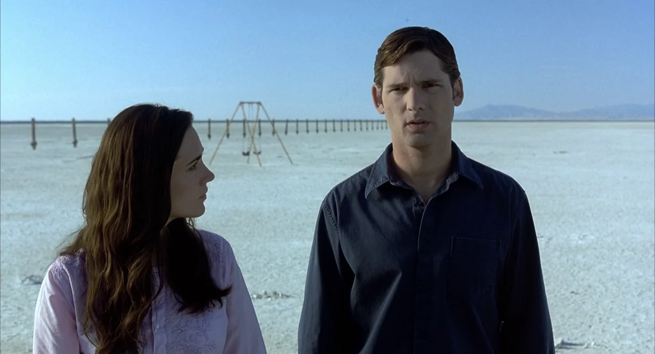 Hulk (2003) movie still: medium — A vast, flat, white salt desert stretches out under a clear blue sky. A man and a woman stand together while a…