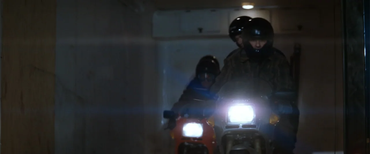 Conspiracy Theory (1997) movie still: medium — A dimly lit industrial container features plywood walls and fluorescent overhead lighting. Two men…