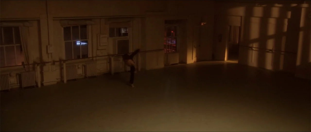 El acto (1989) movie still: wide — A spacious room features hardwood floors, ballet barres, and tall rectangular windows. A man moves through an…