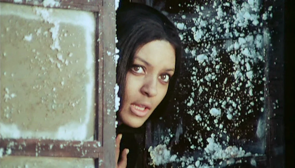The Great Silence (1968) movie still: closeup — A woman looks through a dirty, frosted window frame with textured glass panes. She gazes intently…