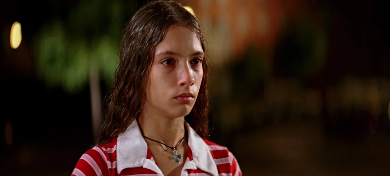 Volver (2006) movie still: closeup — A teenage girl stands outdoors at night with an out-of-focus background. She looks forward while wearing a…