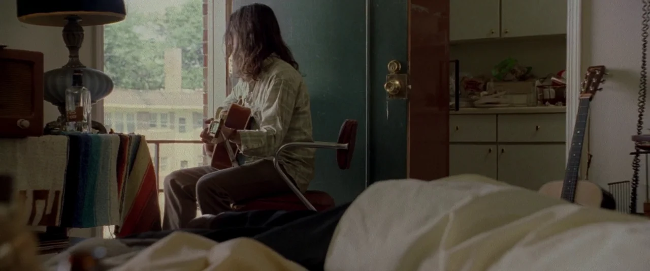 Walk The Line (2005) movie still: medium — An interior space features a person playing guitar in front of an open doorway. Cluttered surfaces with a…