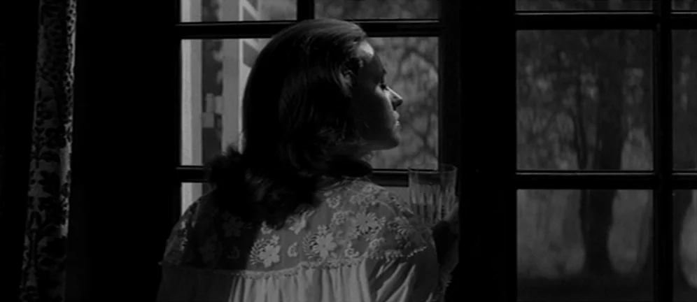 Les Amants (1958) movie still: medium — A dark room with a paneled window looking out at night. A woman in a lace nightgown looks through the window…