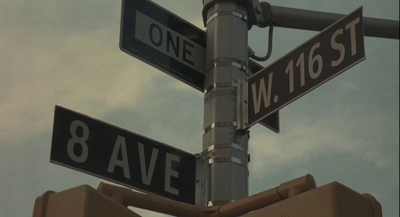 American Gangster (2007) movie still: closeup — A metal signpost stands against an overcast sky at a New York City intersection. Three black street…