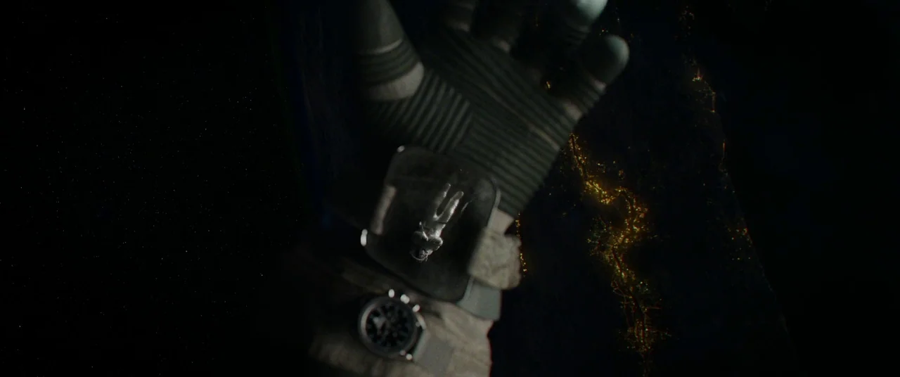 Gravity (2013) movie still: closeup — An astronaut's gloved hand is visible in the foreground floating against the dark space background. The…