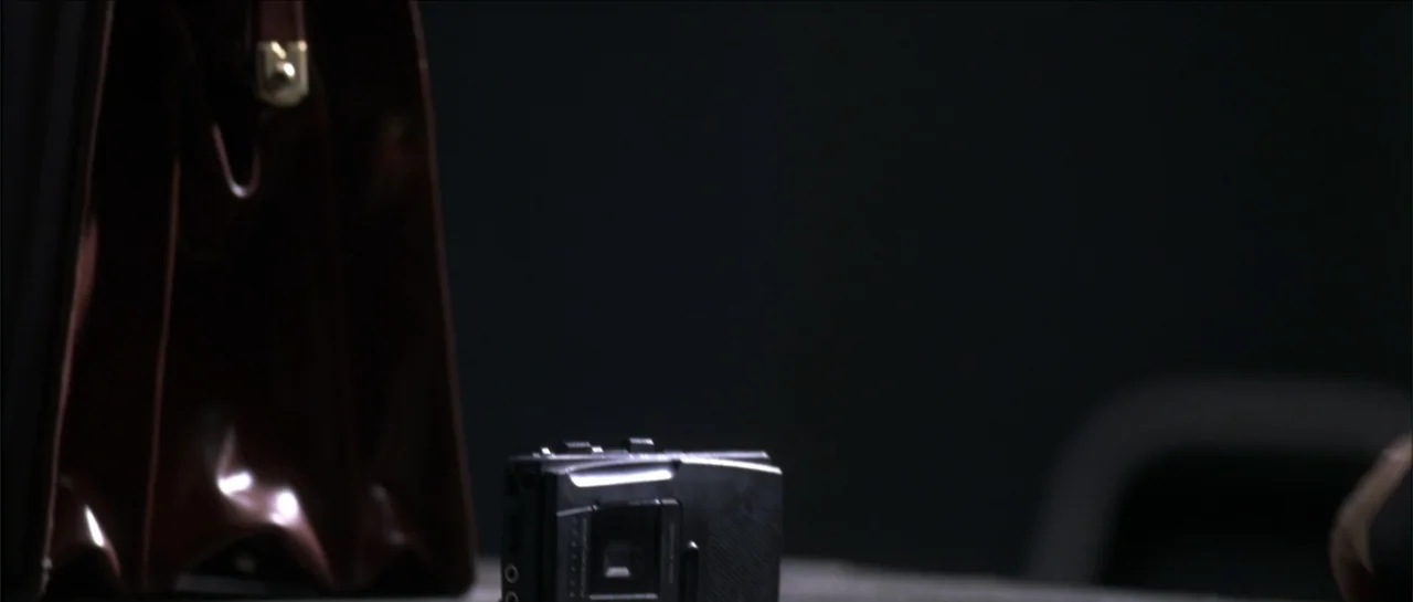Gang Related (1997) movie still: closeup — A dark, nondescript room contains a table with a briefcase and a recorder. A small digital tape recorder…
