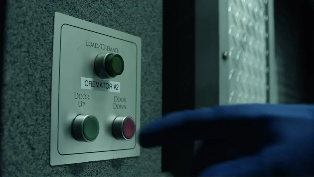 The Cleaner (2021) movie still: closeup — A metallic control panel with three buttons is mounted on a textured grey wall. A hand in a blue medical…