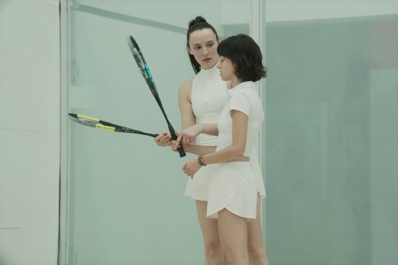 Red Rooms (2023) movie still: medium — A modern, minimalist indoor sports facility features glass walls and bright white surfaces. Two women in…