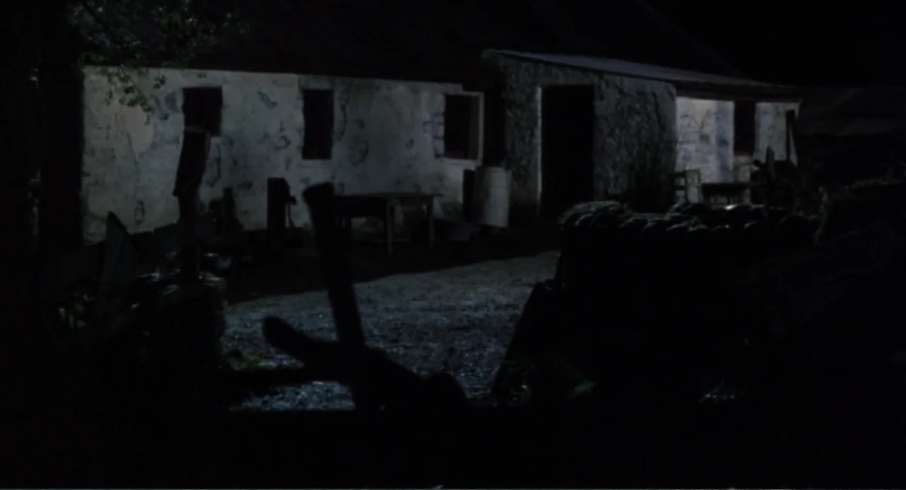 Dancing at Lughnasa (1998) movie still: wide — A rural stone cottage exterior at night features a weathered wall and dark yard. The scene is empty…