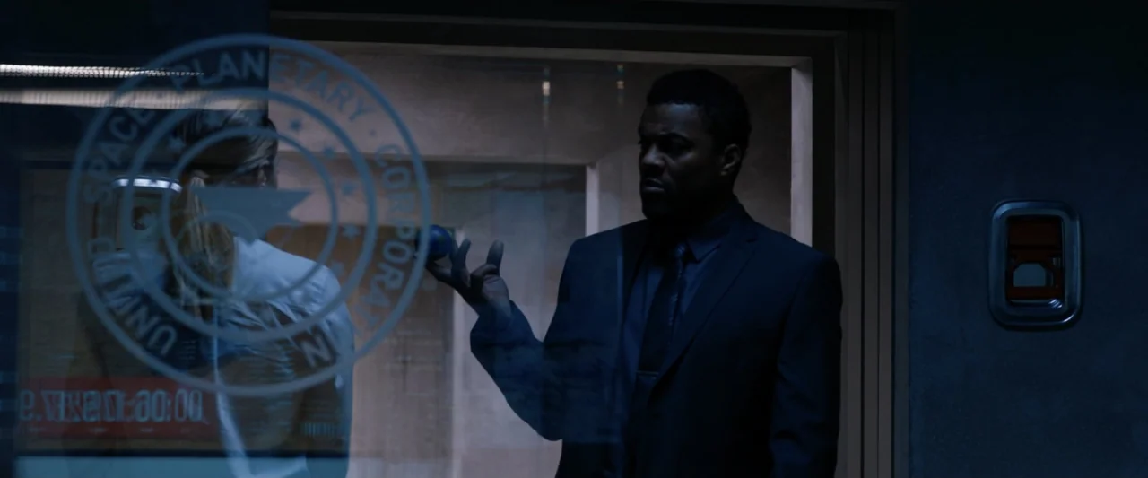 2036 Origin Unknown (2018) movie still: medium — A dimly lit modern office building corridor features a glass pane with corporate branding. A man in…