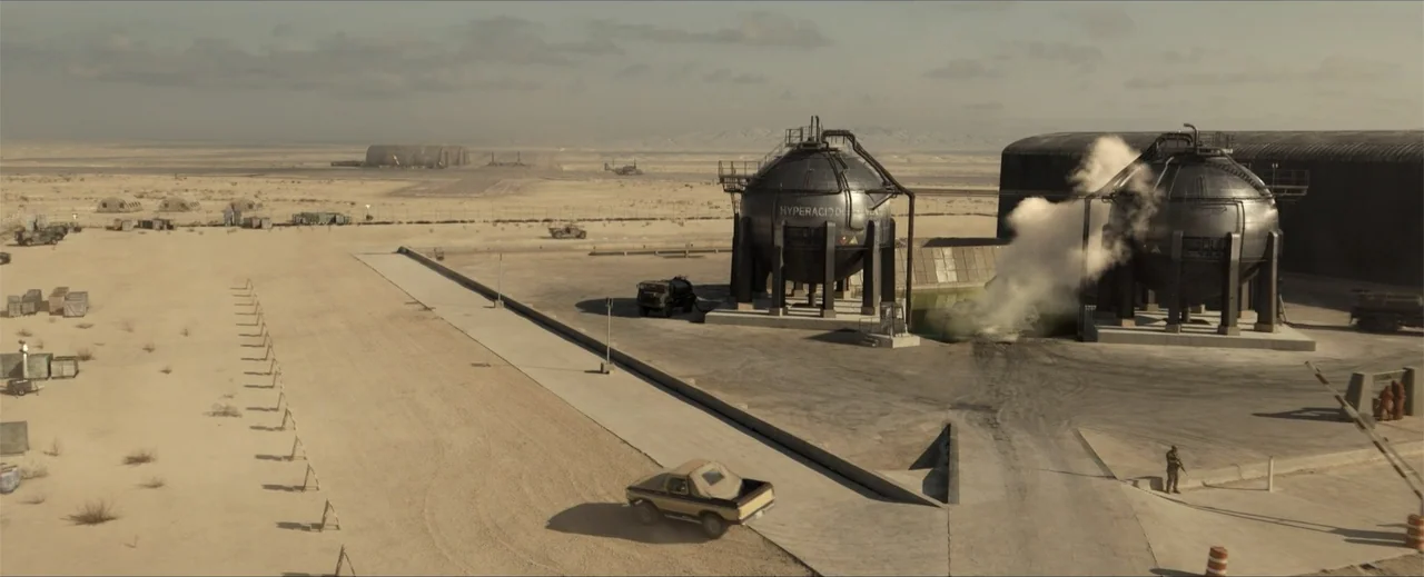 Venom: The Last Dance (2024) movie still: establishing — An industrial facility features large spherical metal storage tanks situated in an arid…