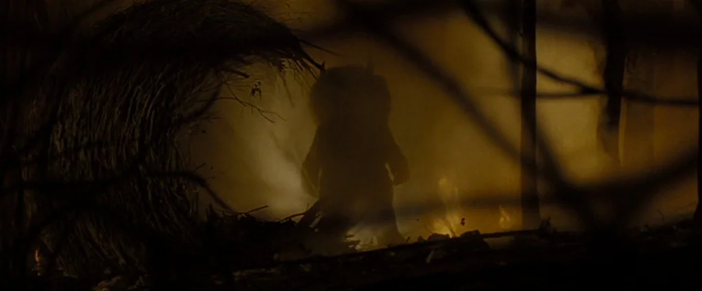 Where The Wild Things Are (2009) movie still: wide — A dark wooded area is filled with thick haze and warm flickering light. A large furry creature…
