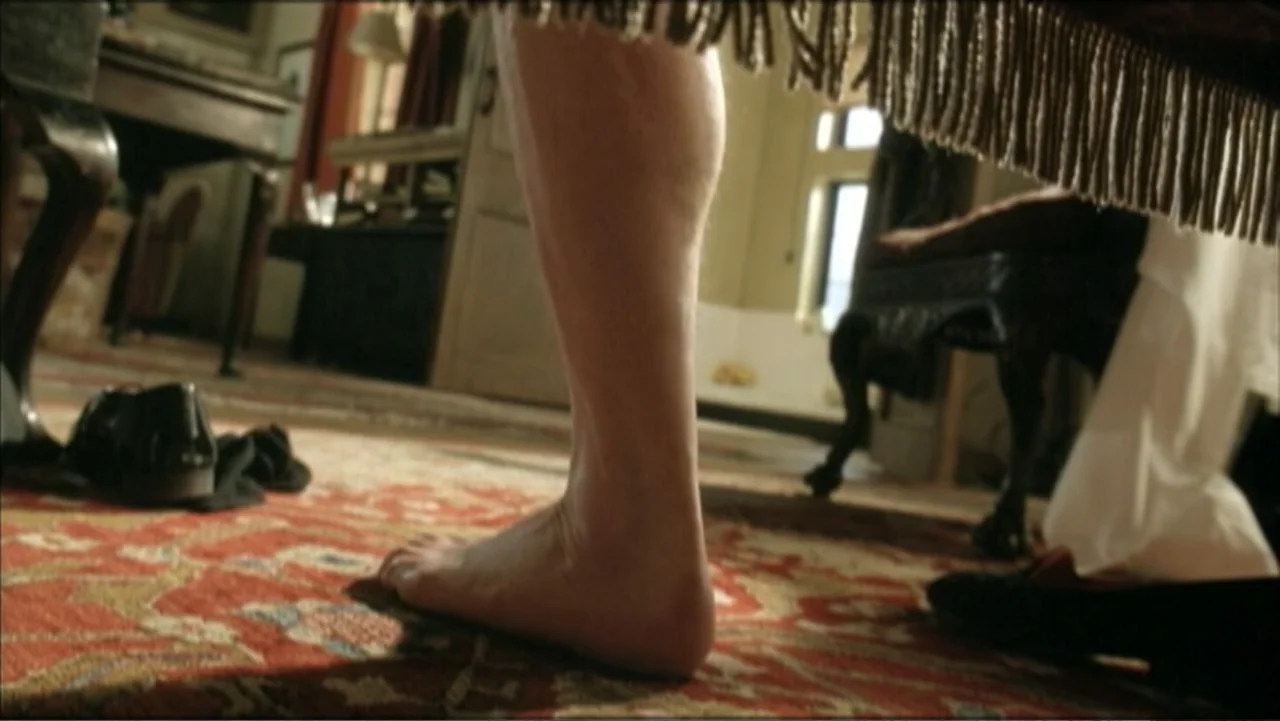 The Gathering Storm (2002) movie still: closeup — A furnished interior space with a patterned rug and dark wooden furniture. A single bare human leg…