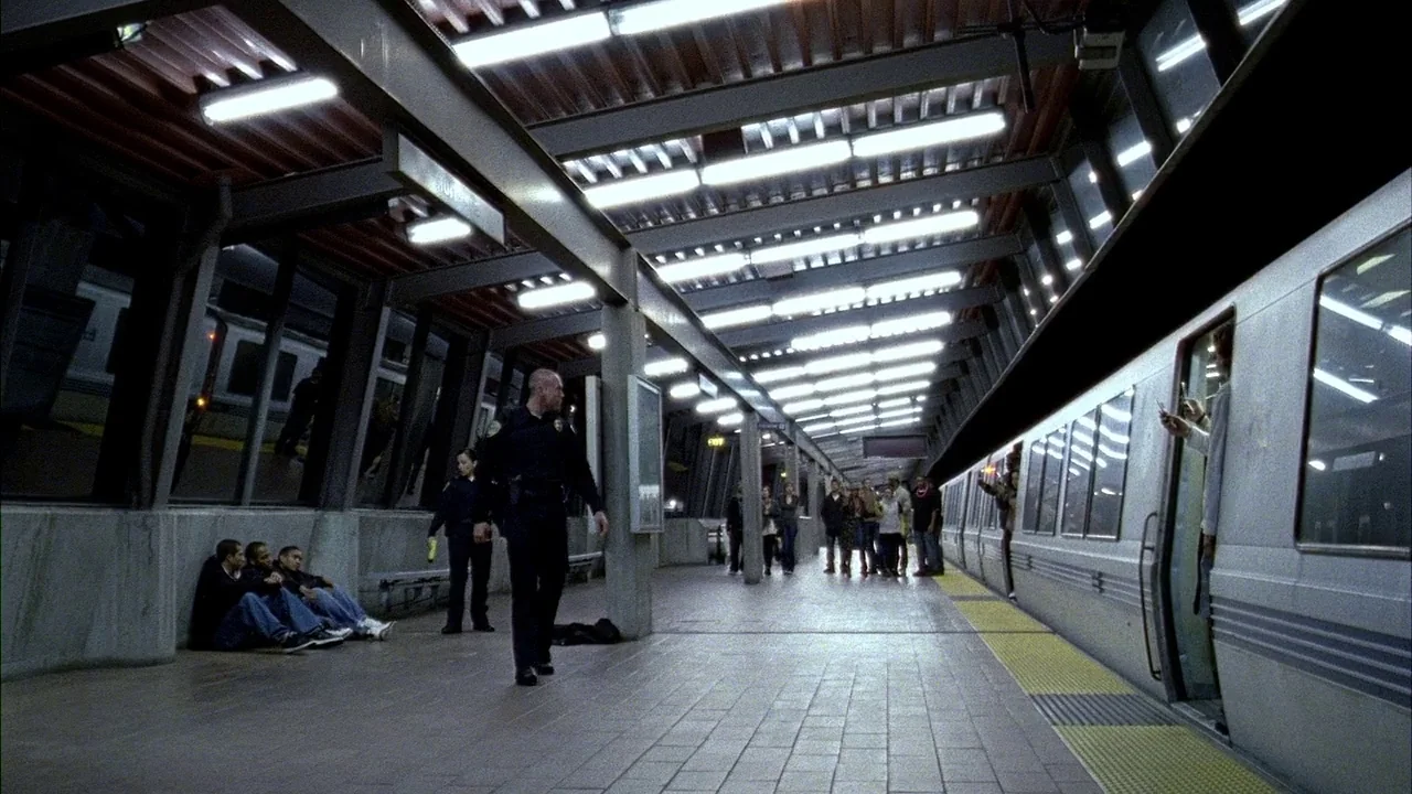 Fruitvale Station (2013) movie still: wide — An industrial subway platform features metal-ribbed ceilings and rows of bright fluorescent lights. A…