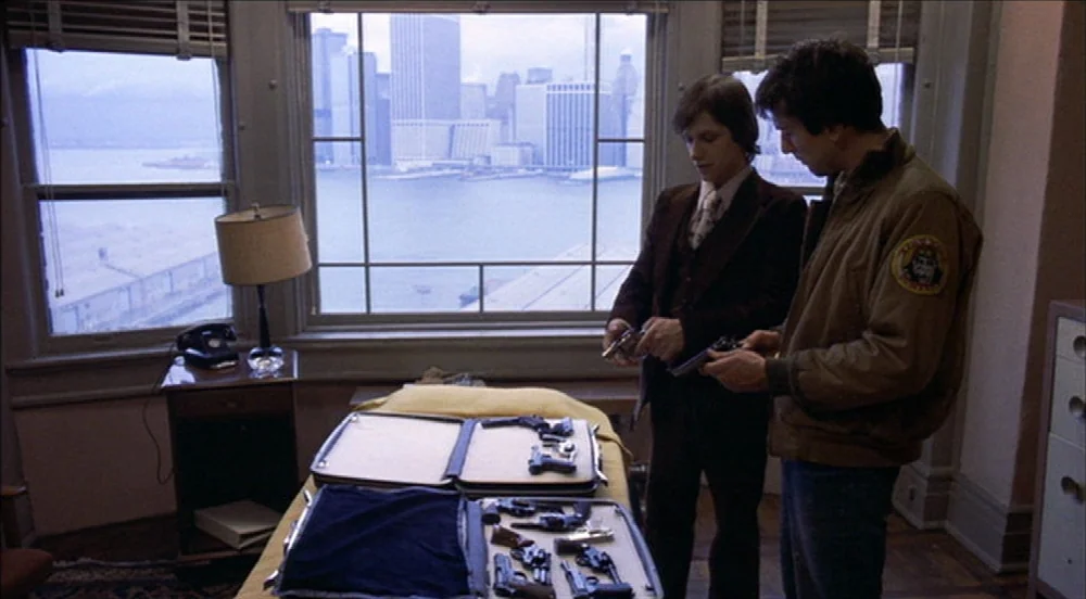 Taxi Driver (1976) movie still: medium — A high-rise apartment overlooks a city waterfront through a large, multi-paned window. Two men stand over a…