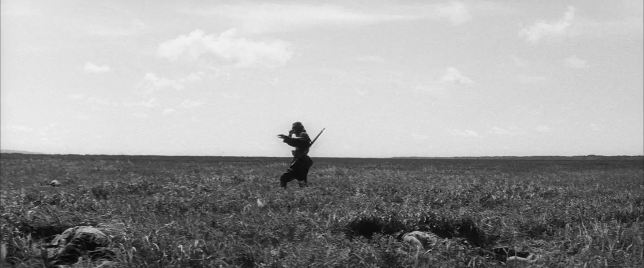 The Human Condition III: A Soldier’s Prayer (1961) movie still: wide — A vast, flat, grassy field under a bright, cloud-filled sky. A single soldier…