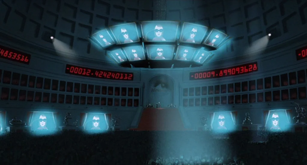 The Congress (2013) movie still: establishing — A vast, dark circular auditorium features tiered seating and walls lined with digital displays. A…