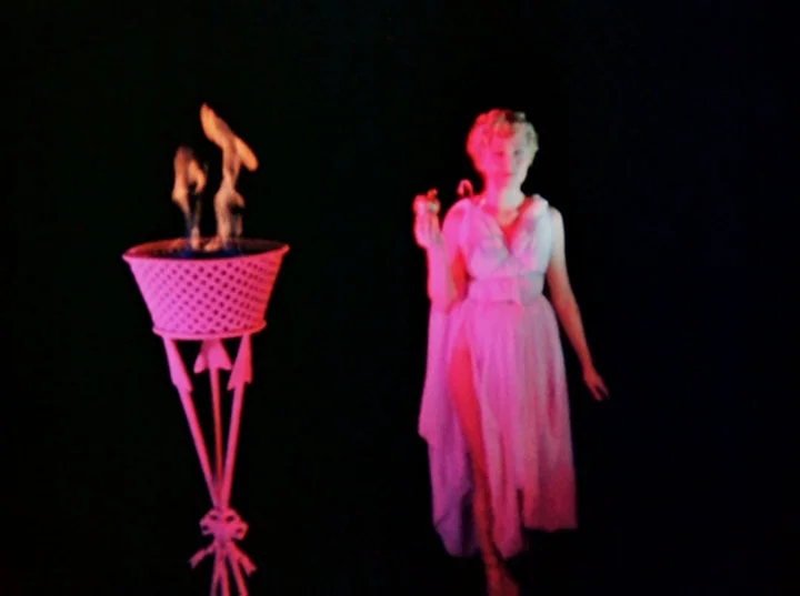 Inauguration of the Pleasure Dome (1954) movie still: fullbody — A woman in a gown stands against a pure black background on a stage. Beside her is…