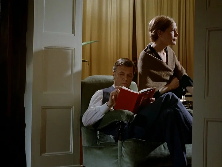 Mother Kusters Goes To Heaven (1975) movie still: medium — A man and woman sit in a green velvet armchair in a paneled room. The man holds an open…