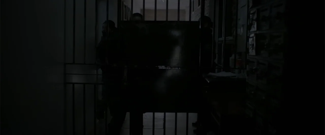 I Trust in You (2016) movie still: medium — A dimly lit narrow stairwell features a heavy metal security gate separating the space. Two figures…