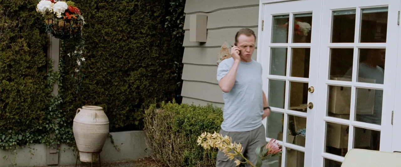 Hector and the Search for Happiness (2014) movie still: fullbody — A residential outdoor area features a tall evergreen hedge and white-framed glass…