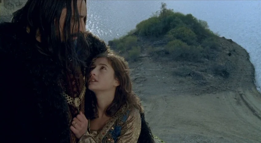 Bluebeard (2009) movie still: medium — A high-angle shot overlooking a lake from a steep, dirt-covered hillside. A man in a dark fur coat stands…