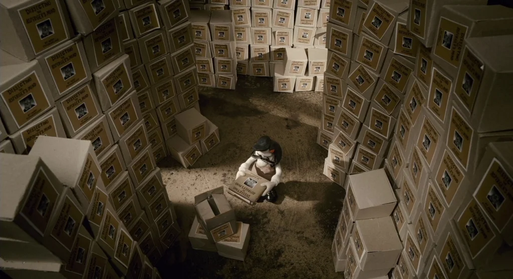 Mary & Max (2009) movie still: wide — A storage room contains towering stacks of cardboard boxes labeled with book covers. A single stop-motion…