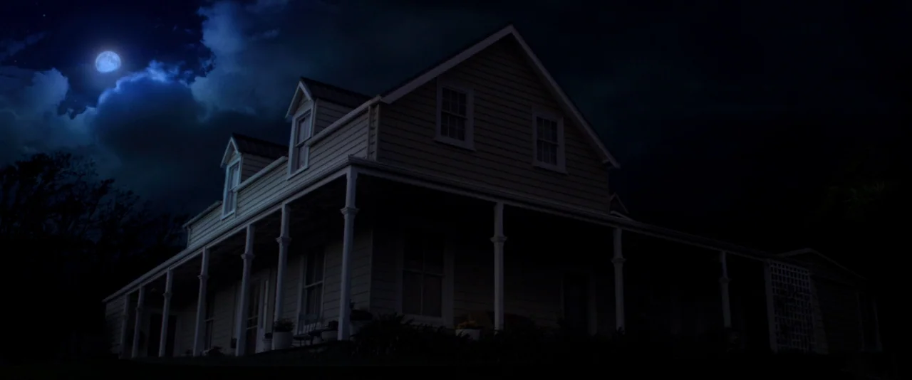 Pearl (2022) movie still: establishing — A wooden farmhouse with a wrap-around porch stands against a dark night sky. The moon glows brightly behind…