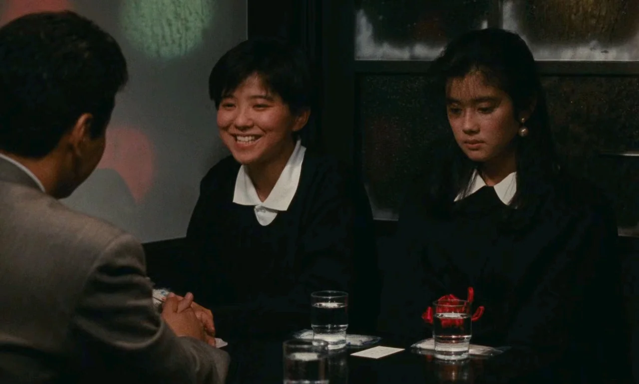 Chizuko’s Younger Sister (1991) movie still: medium — A dimly lit restaurant interior features dark wood paneling and decorative circular wall…
