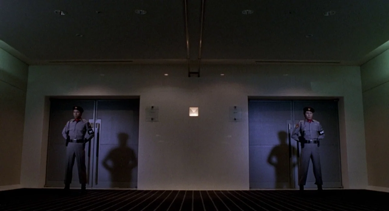 Godzilla vs. Destoroyah (1995) movie still: wide — A dark, minimalist hallway features two sets of large metal double doors side by side. Two…