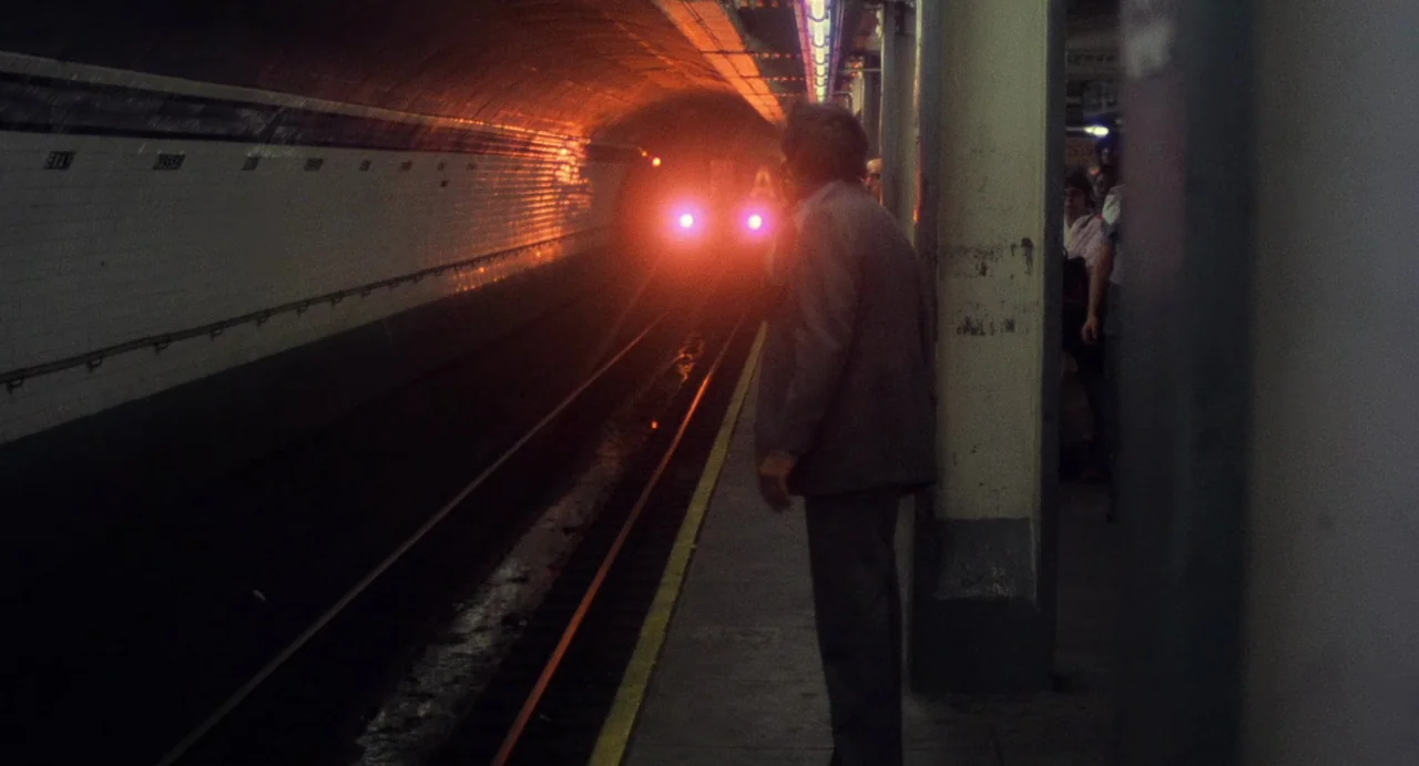 God Told Me To (1976) movie still: fullbody — A dimly lit New York City subway platform with tiled walls and grimy concrete columns. An older man in…