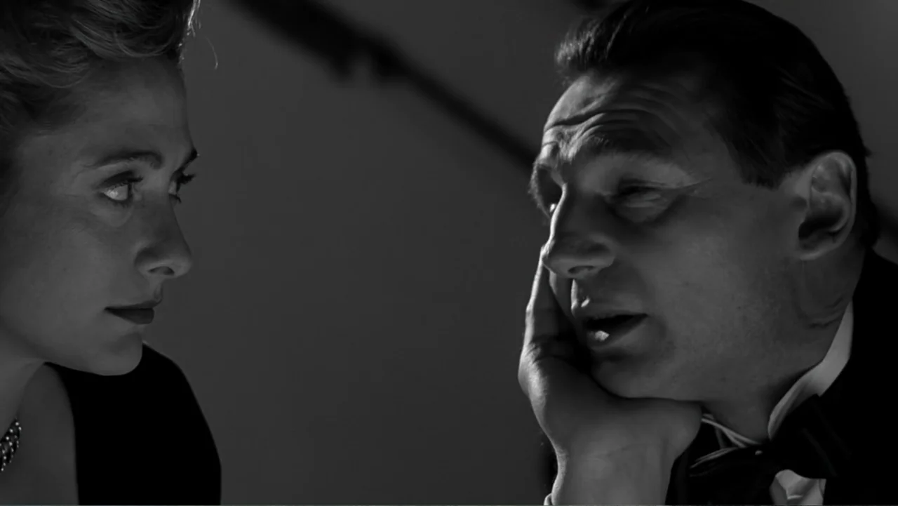 Schindler's List (1993) movie still: closeup — A dimly lit room provides the backdrop for a formal encounter between two people. A man sits in a…